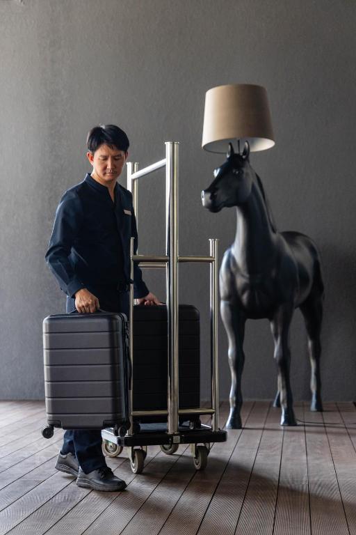 A hotel attendant stands with a luggage trolley beside a distinctive horse statue.