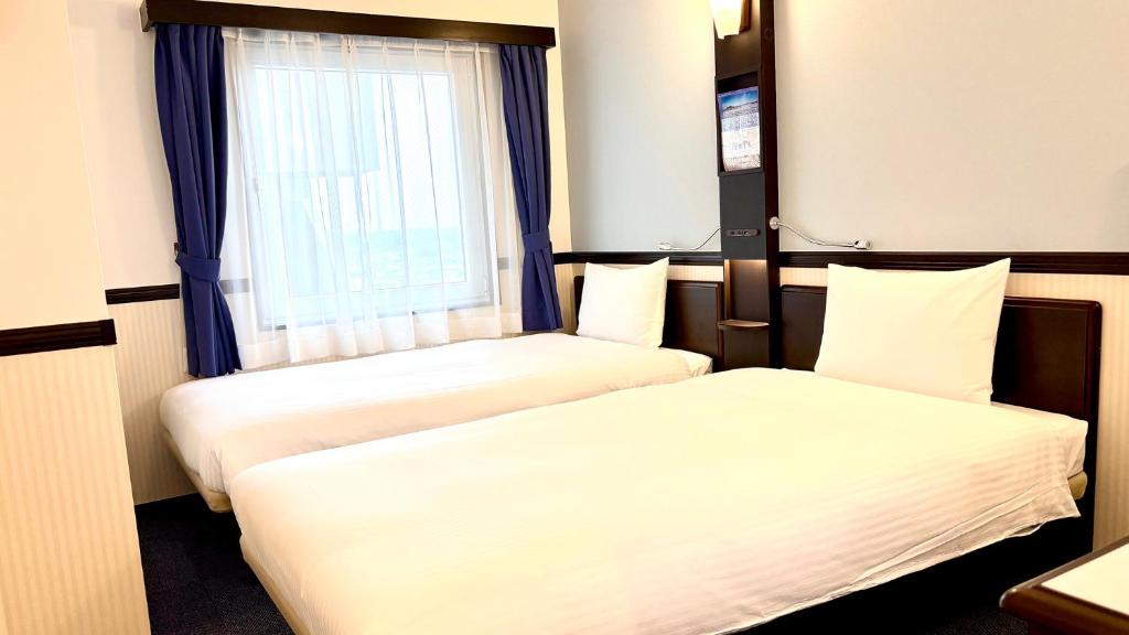 Toyoko Inn Chiba Shin kamagaya Ekimae في Kamagaya: سريرين في غرفة فندقية بها نافذة