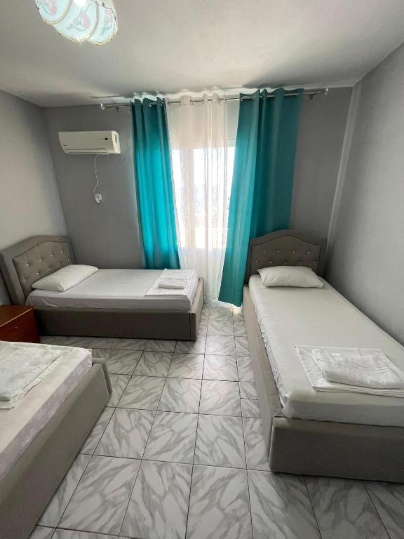 two beds in a room with blue curtains at Hotel Gjika in Sarandë