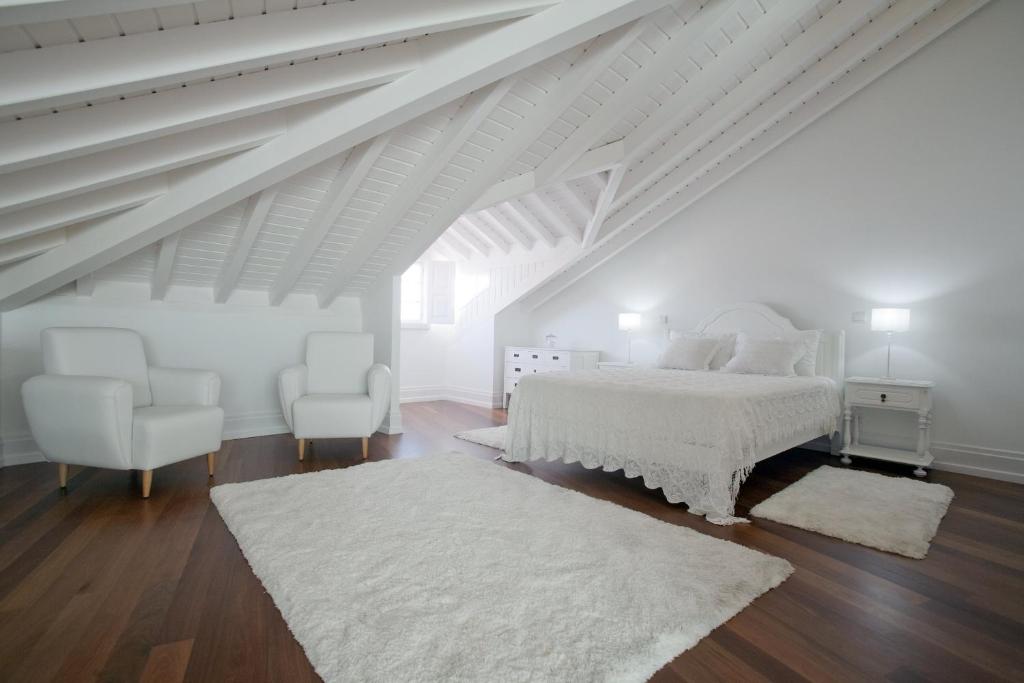 a white bedroom with a white bed and two chairs at Mercearia da Vila in Ponte de Lima