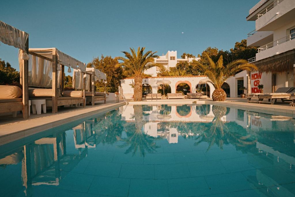 a swimming pool in a resort with palm trees and buildings at Sunset Oasis Ibiza Adults Only - New Rooms 2025 in San Antonio Bay
