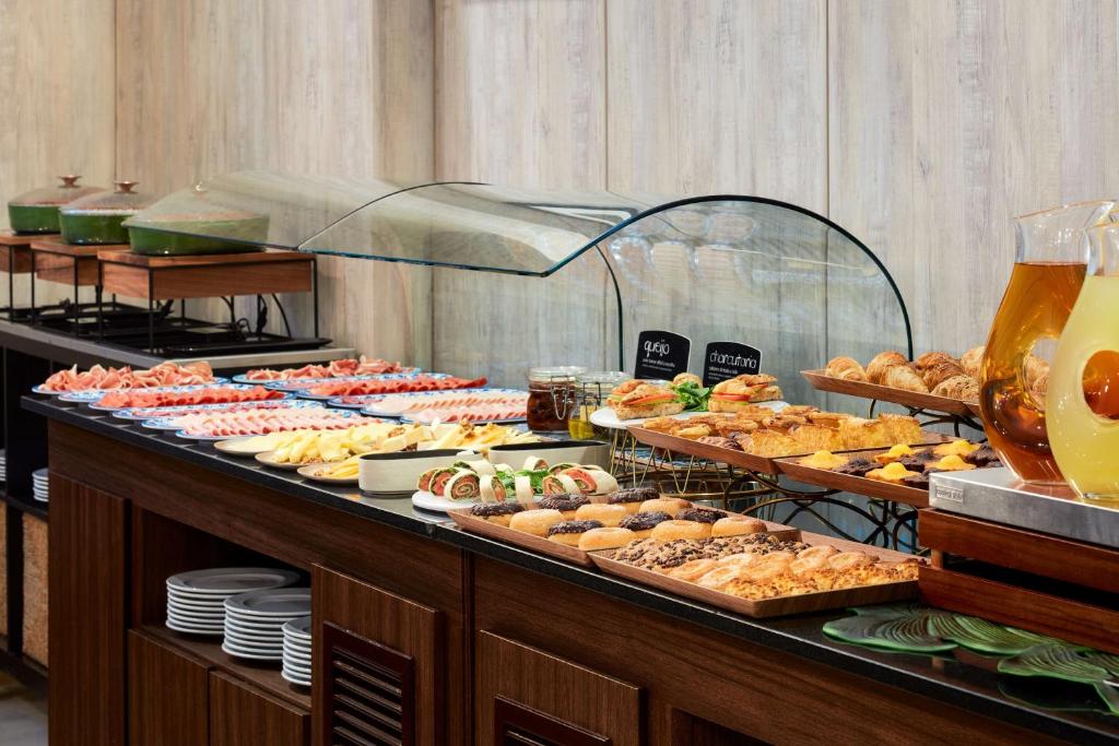 A long breakfast buffet with pastries, cold cuts, fruit, bread and drinks.