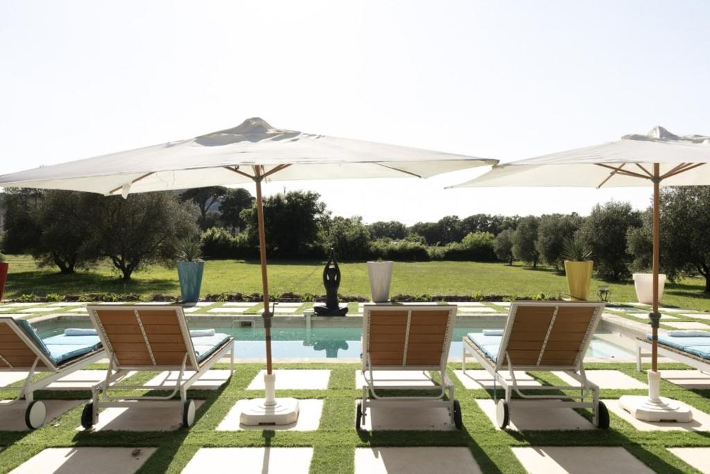 eine Gruppe von Stühlen und Sonnenschirmen neben einem Pool in der Unterkunft Bastide Blanche in Les Arcs sur Argens