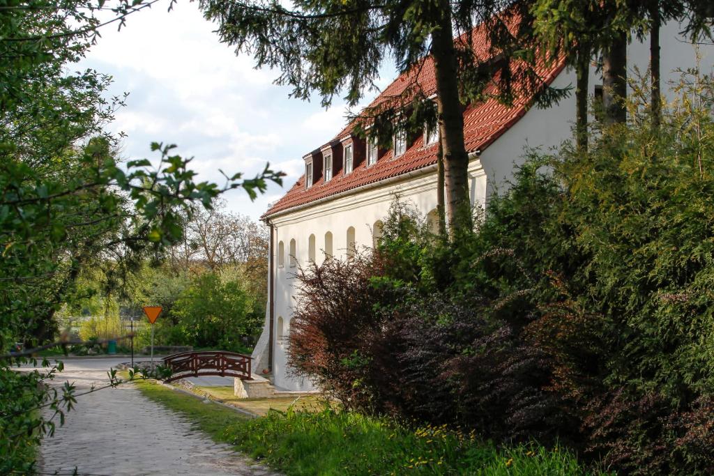 um edifício branco com um telhado vermelho e um banco em Spichlerz Bliźniaczy em Kazimierz Dolny