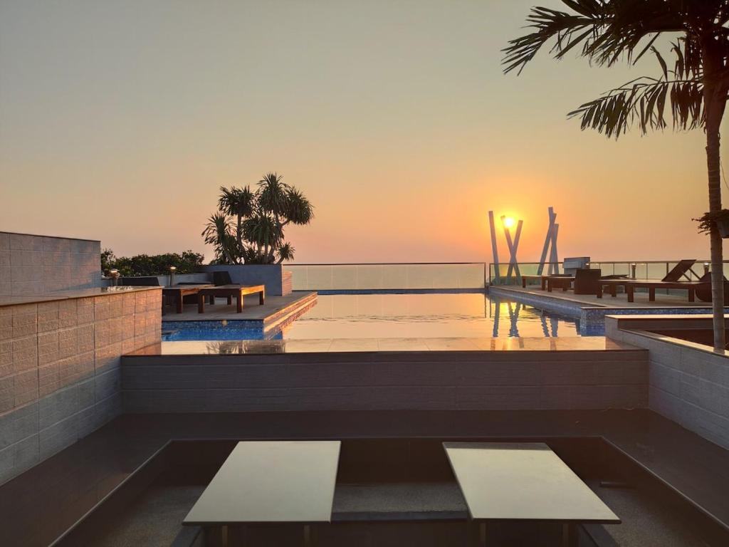 a sunset over a swimming pool with benches and palm trees at The Gallery Condominium B in Jomtien Beach