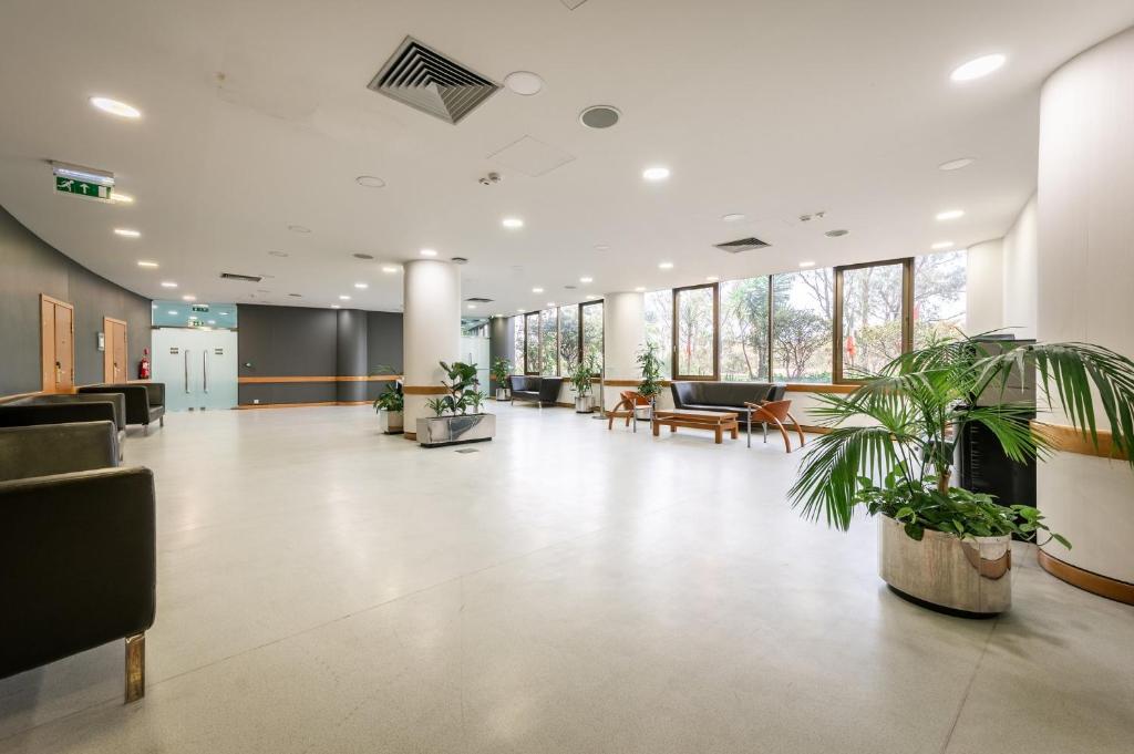 A bright, open hotel lobby with window-side seating and abundant plants.
