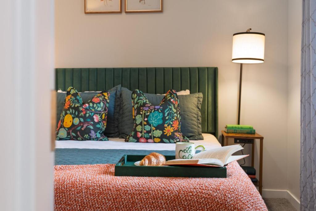 a bed with a green headboard with a book and a coffee mug at Le Nid Trailside 1BD Close to Beach Downtown in Traverse City