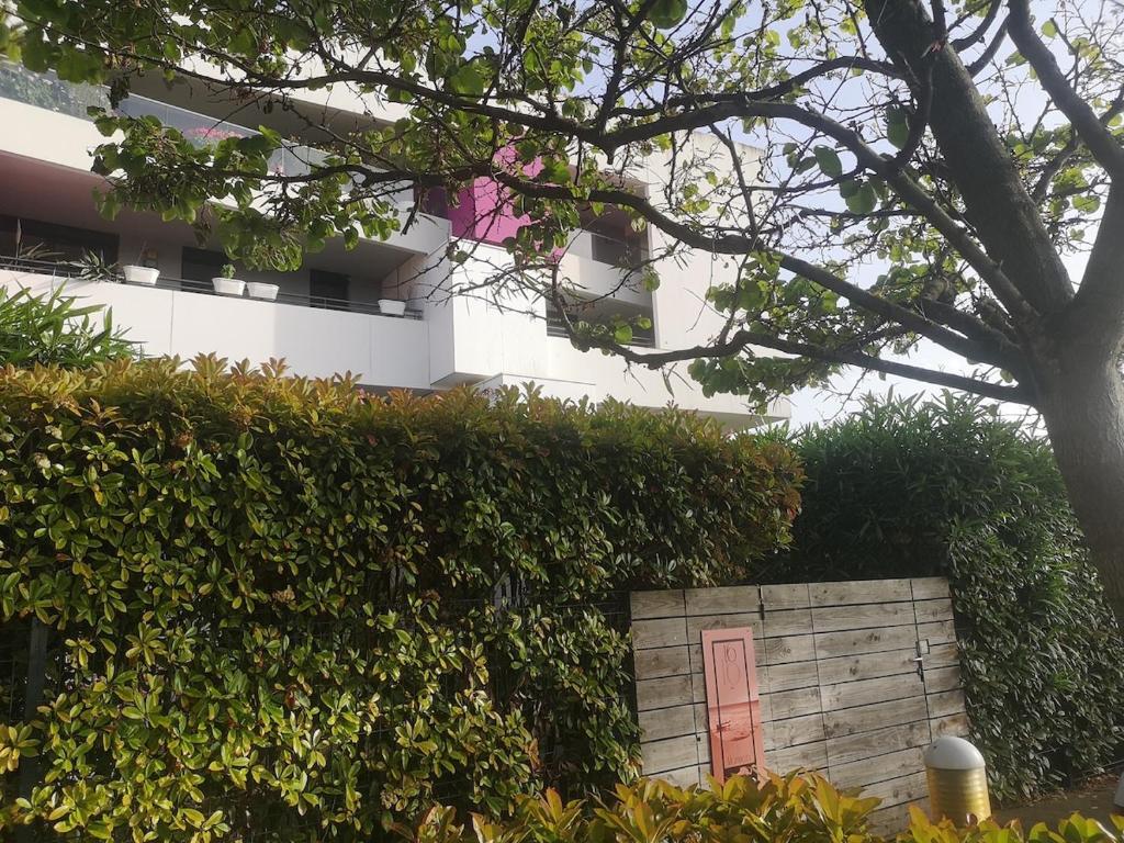 un bâtiment avec une porte rouge derrière une haie dans l'établissement appartement 2 pieces avec parking ds résidence, à Palavas-les-Flots