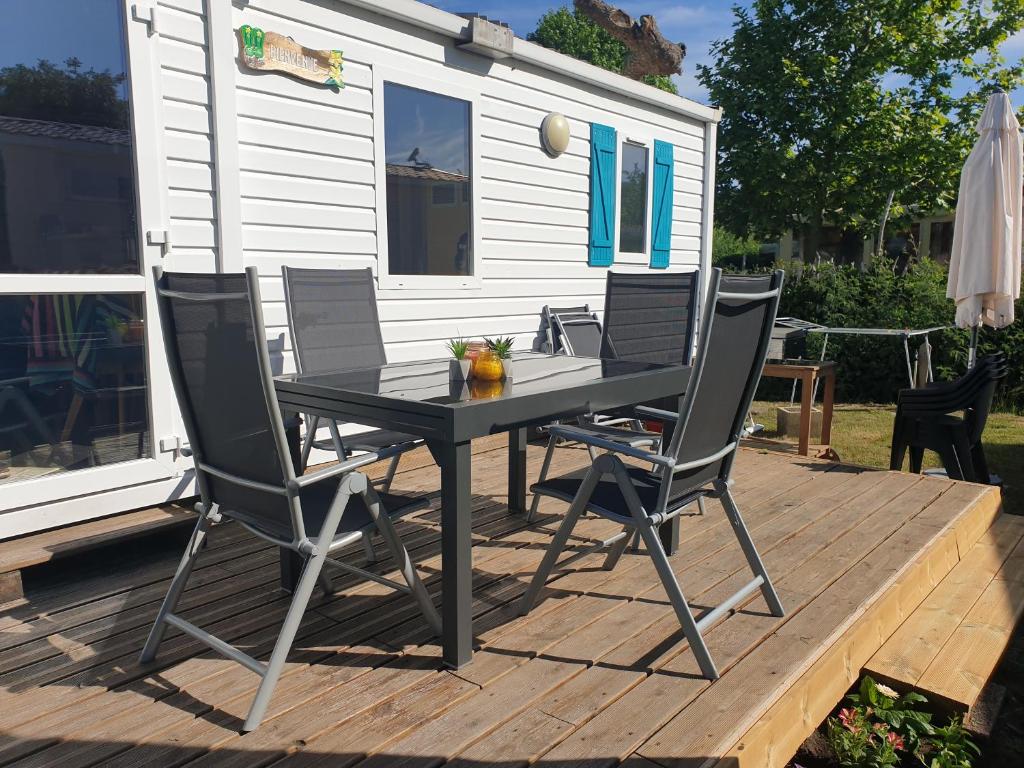 une table et des chaises noires sur une terrasse avec une maison dans l'établissement Biscarrosse lac Mobil home tout confort, à Biscarrosse
