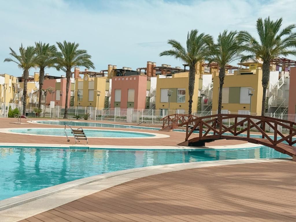 a bridge over a pool with palm trees and buildings at Ático Dúplex con Jacuzzi en Vera Playa y parking cubierto enorme in Vera