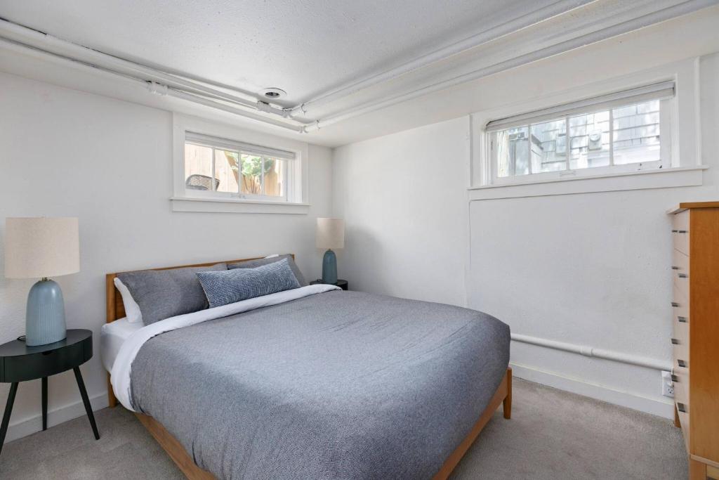 a white bedroom with a bed and two windows at Stylish Daylight Basement Apartment- Patio + Grill in Seattle