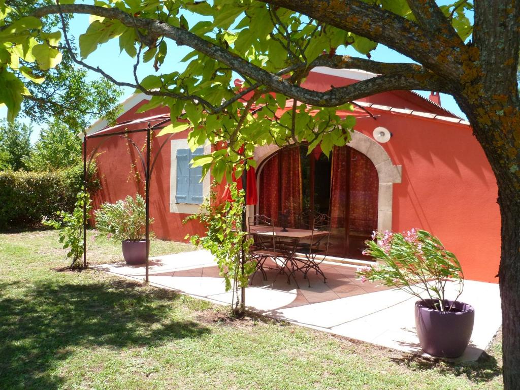 a red house with a table and chairs under a tree at Luberon & Lavandes in Roussillon