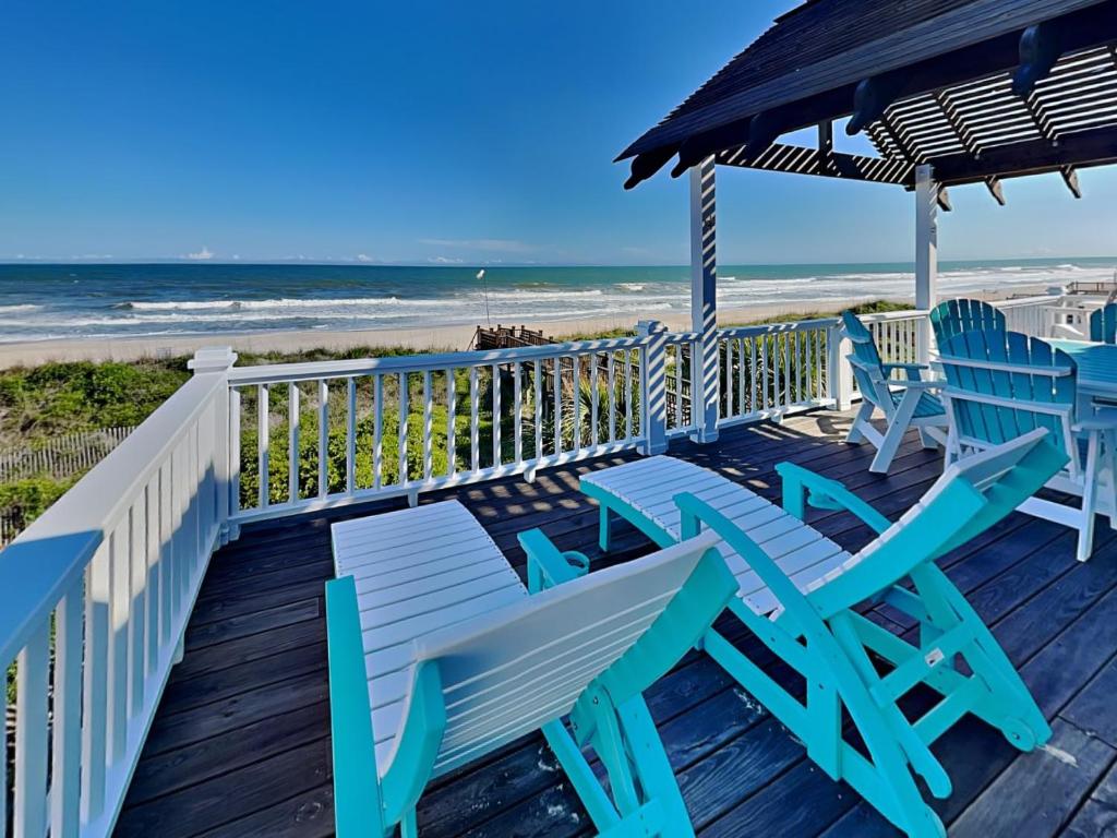 a deck with blue chairs and an umbrella and the beach at Blue Me A Wave in North Topsail Beach