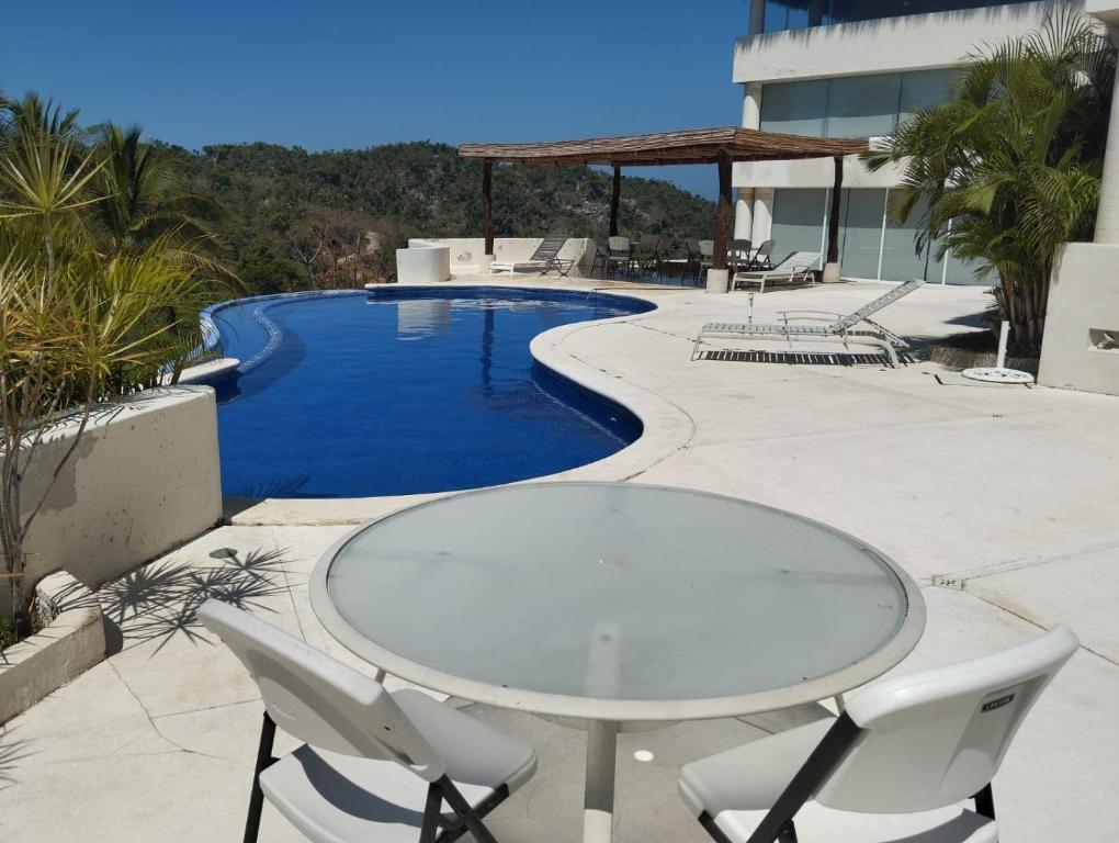 einen Glastisch und Stühle neben einem Pool in der Unterkunft Exclusivo Alojamiento en Real diamante in Acapulco