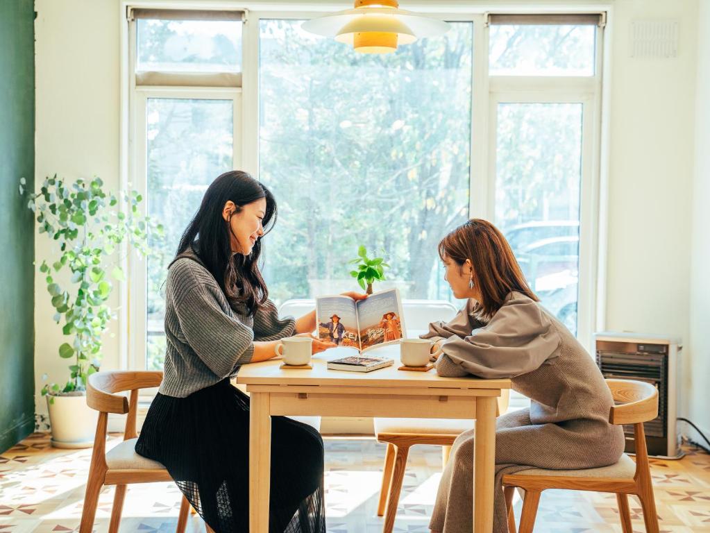 two women sitting at a table drinking coffee at ゲストハウスVACILANDO in Chitose