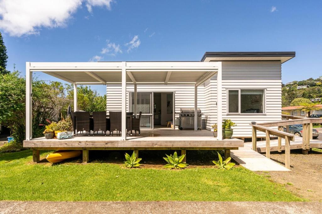 a small white house with a porch and a deck at Kombi Cottage Fully accessible in Tairua