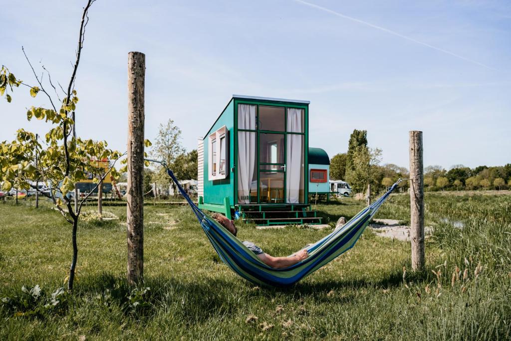 a person laying in a hammock in front of a tiny house at Hihahut De Tuureluur in Oud-Ade