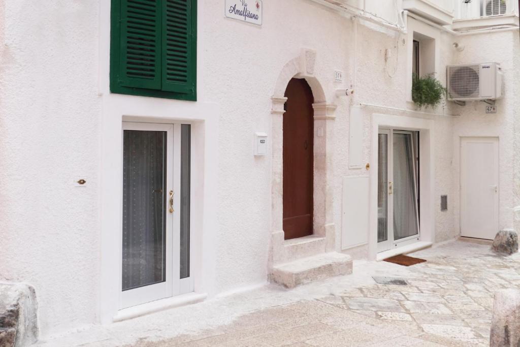a white building with green shutters on a street at La Vitagira in Monopoli