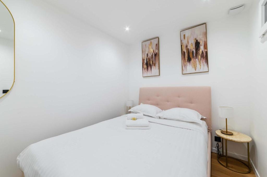 a white bedroom with a bed and two pictures on the wall at Escapade urbaine Appartement Mairie des lilas in Les Lilas