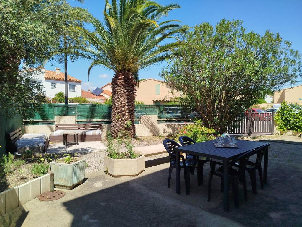 une table et des chaises dans une cour avec un palmier dans l'établissement Rez de jardin pour ce T3 spacieux proche plage et commerces - 4BERNA1, à Saint Cyprien Plage