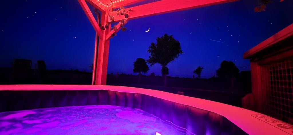 un bain à remous avec éclairage violet dans une arrière-cour la nuit dans l'établissement La Luna - Tiny House Spa - Romantique & Nature, à Saint-Yan