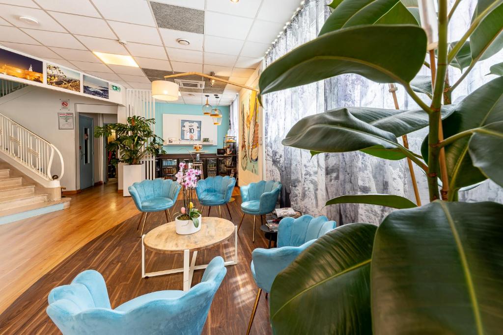 une salle d'attente avec des chaises bleues, une table et une plante dans l'établissement ibis Styles Marseille Centre Prado Place Castellane, à Marseille