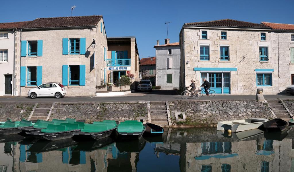 a car parked next to a canal with boats and buildings at Hotel Au Marais in Coulon