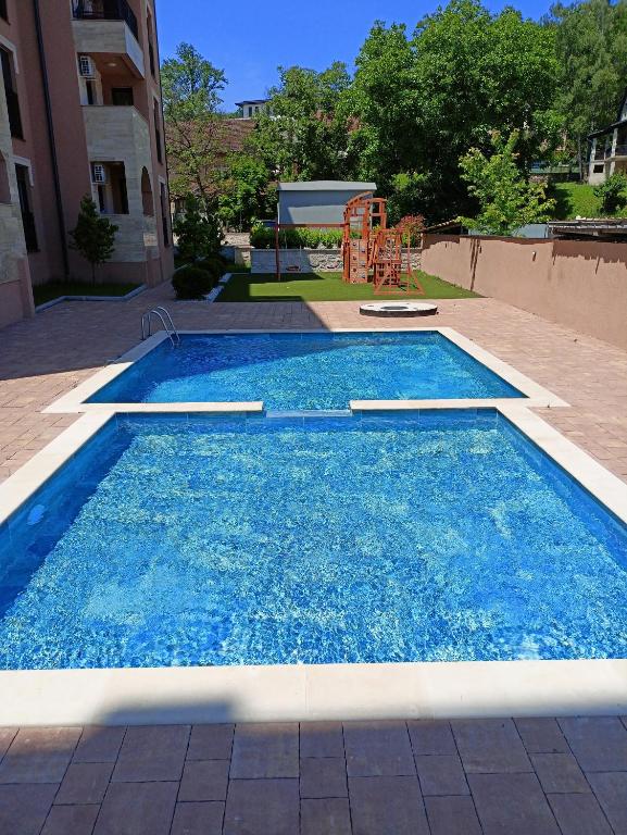 a swimming pool with blue water and a playground at Larso Lux, free swimming pools in Vrnjačka Banja