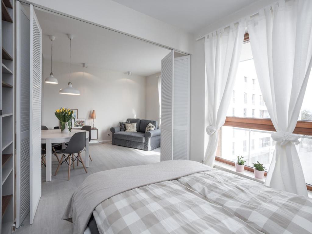 a white bedroom with a bed and a table at Apartament z widokiem na dworek in Gdańsk