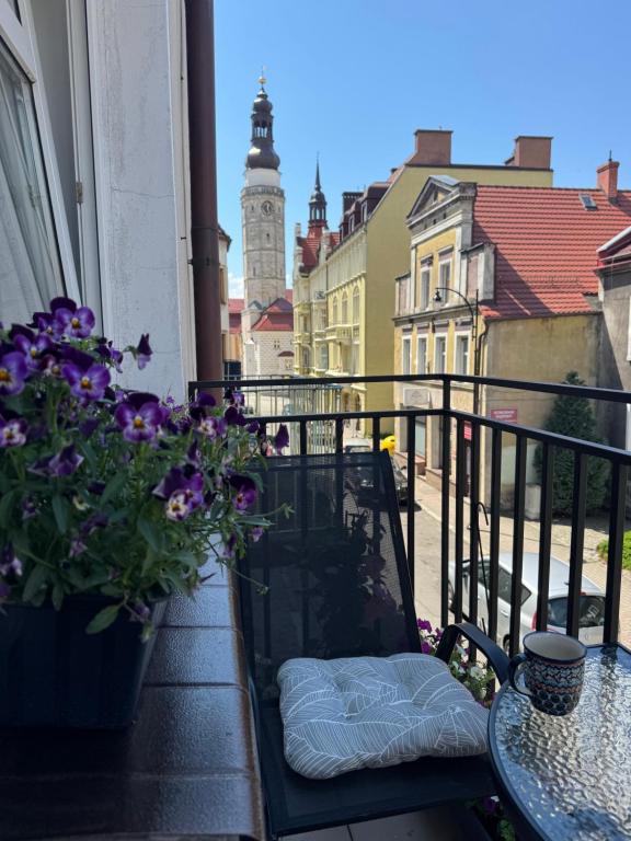 a balcony with a bench and flowers and a clock tower at Apartament Vikicentrum in Bolesławiec