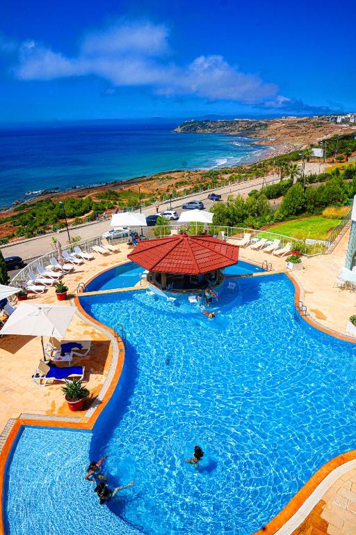 a large swimming pool with a red umbrella and the ocean at Hotel Farah Tanger in Tangier