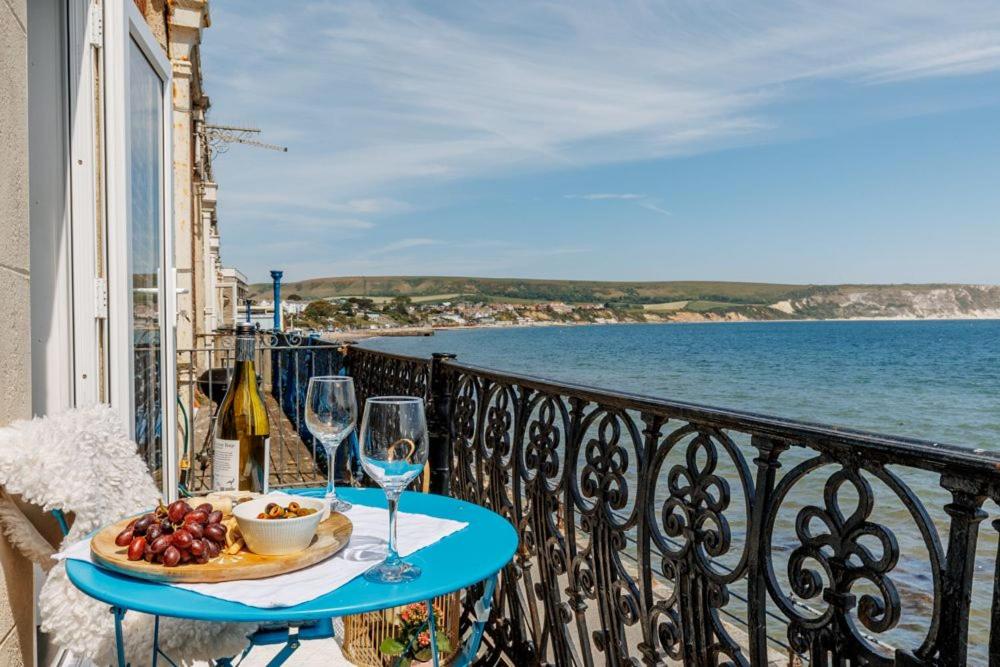 a table with a plate of food and wine glasses on a balcony at Balcony Apartment in Swanage