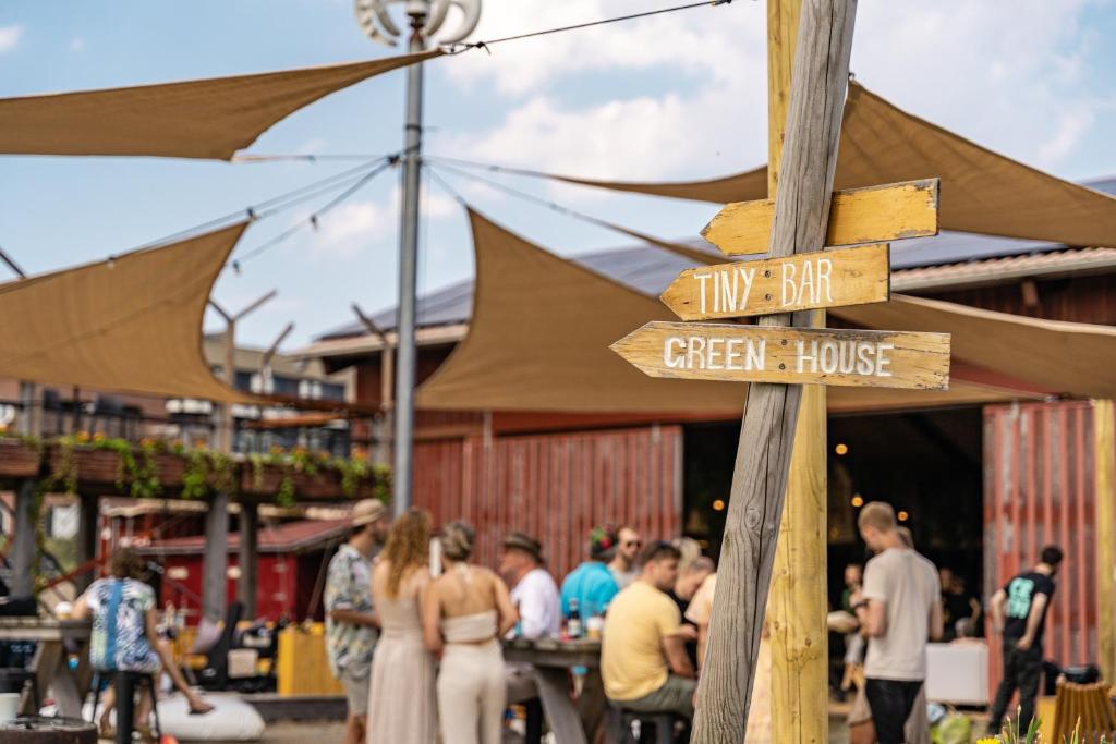 a wooden sign for a green house with people standing outside at Basecamp Tiny House Eco-resort IJmuiden in IJmuiden