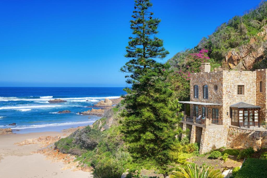 Una casa vieja en la playa junto a un árbol. en Buccara Noetzie - Honeymoon Castle, en Knysna