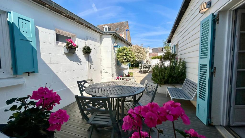 une terrasse avec une table, des chaises et des fleurs roses dans l'établissement Cabane du Pêcheur, maison avec extérieur, au Crotoy