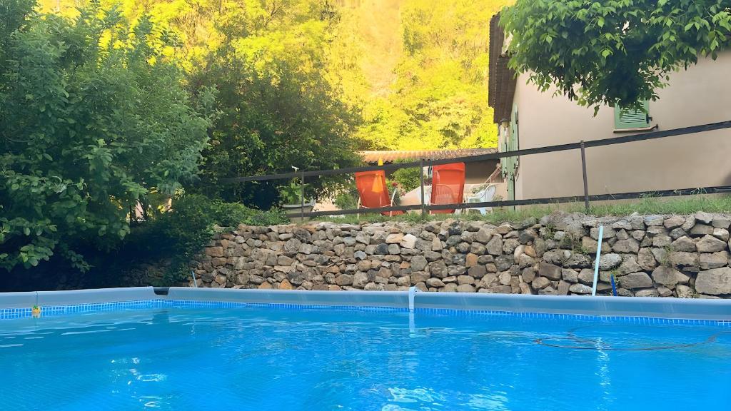 a swimming pool next to a stone wall and a house at Bastidon les Oliviers in Belgentier