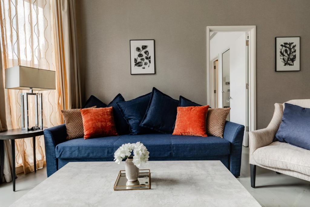 High Street Kensington Apartments في لندن: غرفة معيشة مع أريكة زرقاء ووسائد برتقالية
