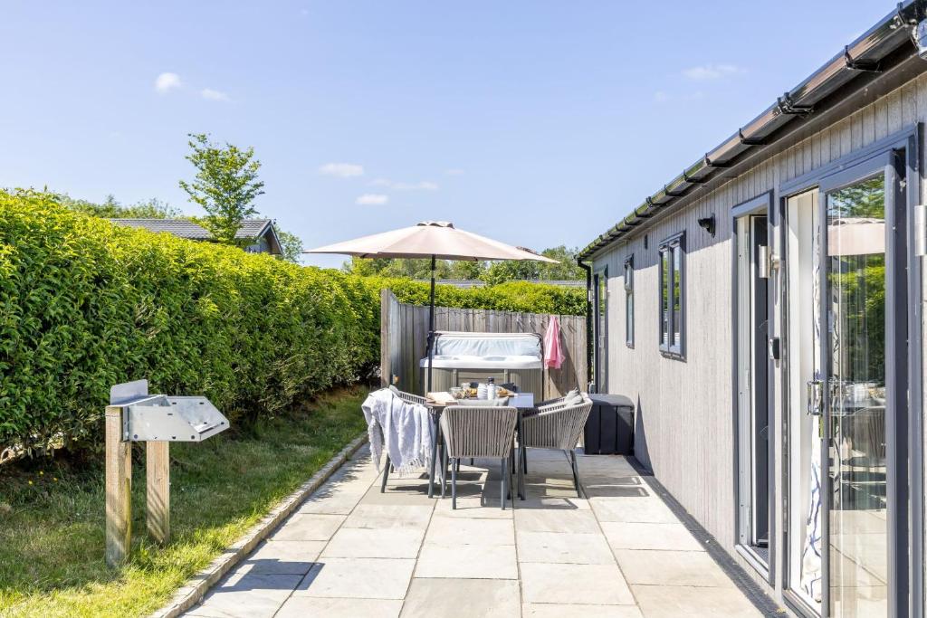 a patio with a table and chairs and an umbrella at Hazel Lodge, 27 Roadford Lake Lodges in Lifton