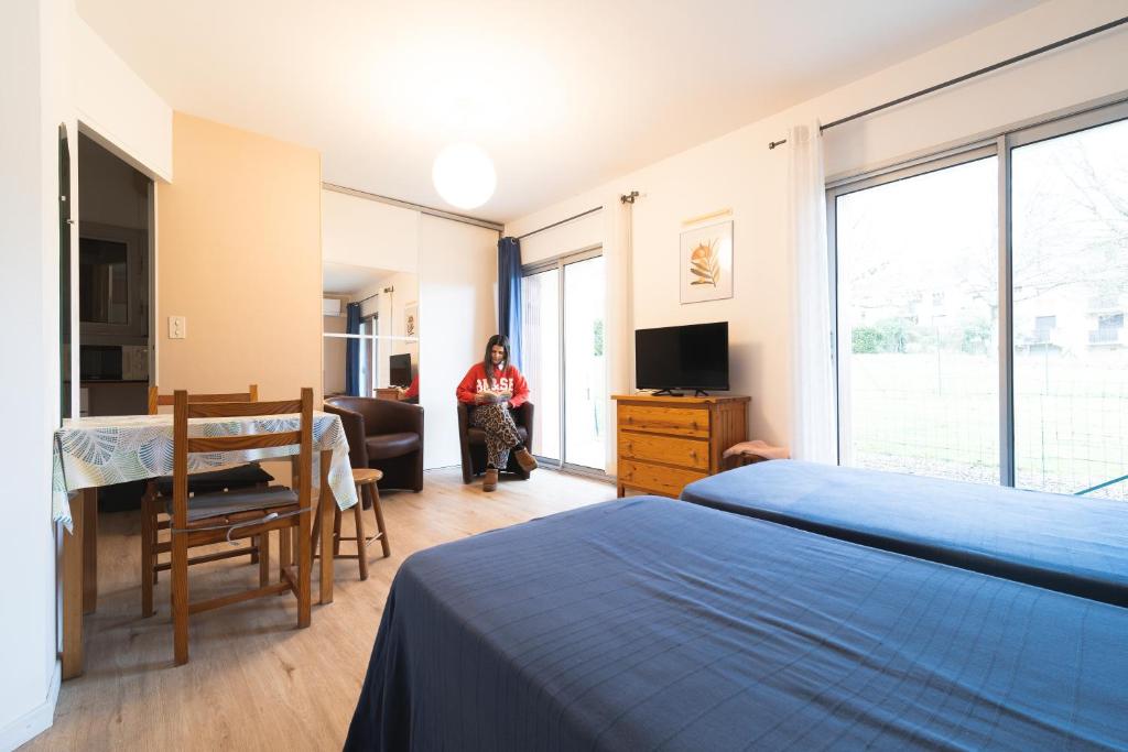 a woman in a bedroom with a bed and a desk at Les Mimosas - App 07 - Appartement Cosy Clim Balcon 1er étage in Cazaubon