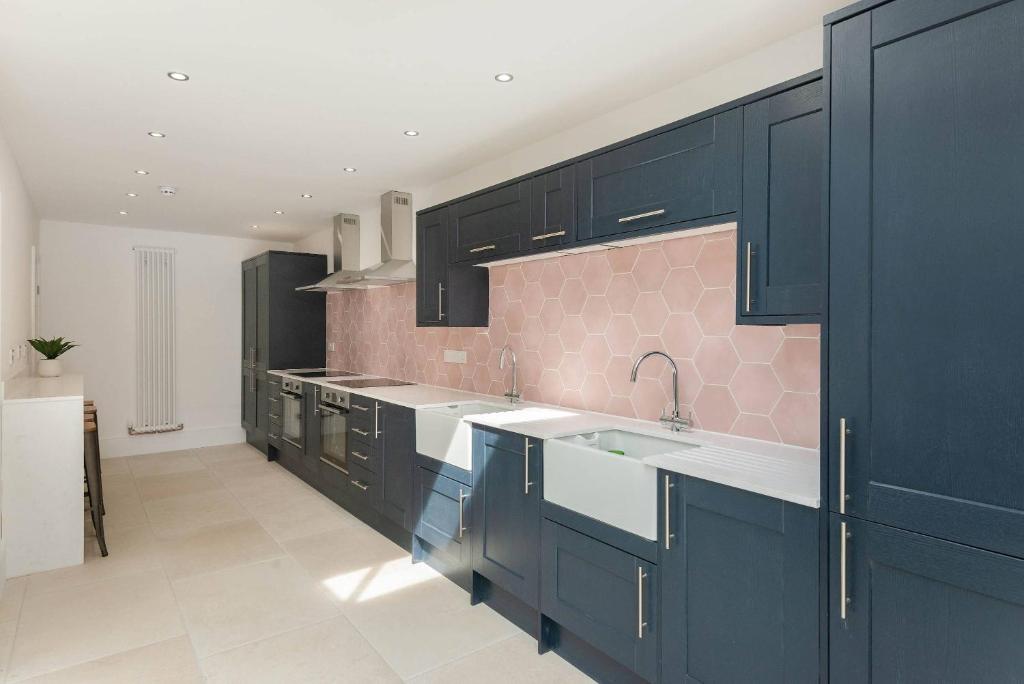 a kitchen with black cabinets and a pink tile wall at Spacious House Private Parking & Garden in Gloucestershire
