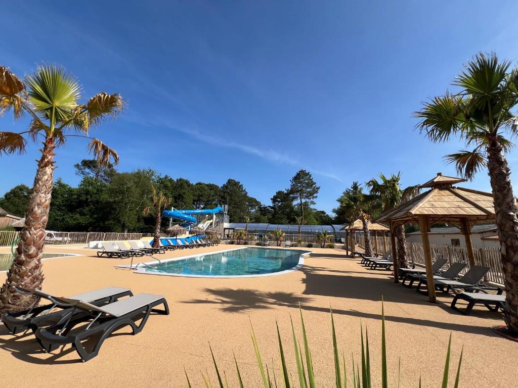 - une piscine avec des chaises et des palmiers dans un complexe dans l'établissement CAMPING LES OURMES, à Hourtin