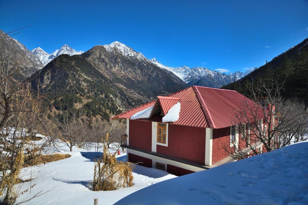 a red house in the snow with mountains in the background at Himalaya Vista - 1km Uphill Hike from Main Road in Harsil