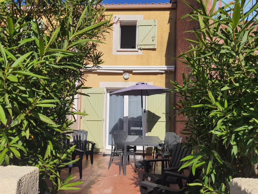 un patio avec une table, des chaises et un parasol dans l'établissement Maison climatisée 2 chambres idéalement située Narbonne plage, à Narbonne-Plage