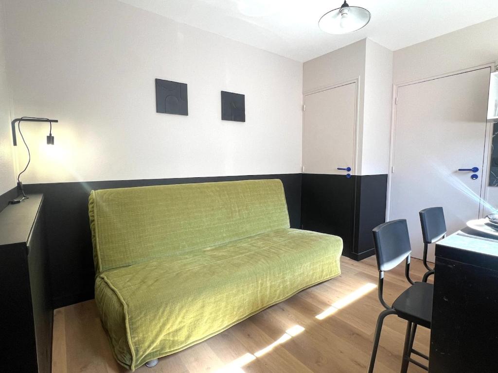 ein grünes Bett in einem Zimmer mit einem Schreibtisch und Stühlen in der Unterkunft Studio en rdc - hyper centre Dol de Bretagne in Dol-de-Bretagne