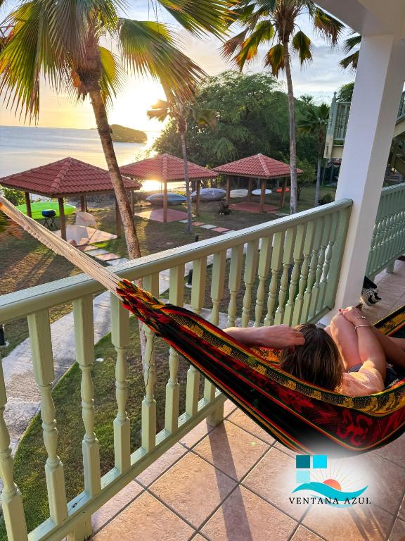 a woman laying in a hammock on a balcony overlooking the beach at Condo Ocean View from Balcony Swimming Pool Playa Sucia in Cabo Rojo