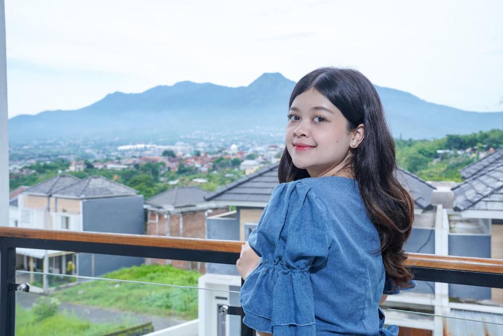 eine junge Frau steht auf einem Balkon mit Bergen im Hintergrund in der Unterkunft Villa Safira Batu in Batu