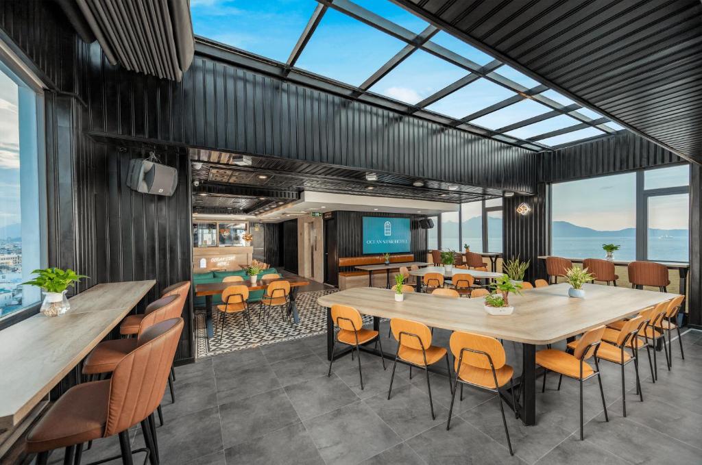 A bright dining area with communal tables, orange chairs, skylights and a broad coastal view.