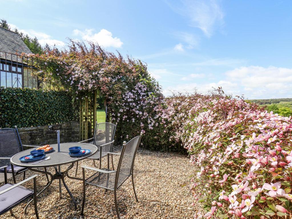 een terras met een tafel, stoelen en een bloemenmuur bij Wayside Farm Cart Cottage in Scarborough