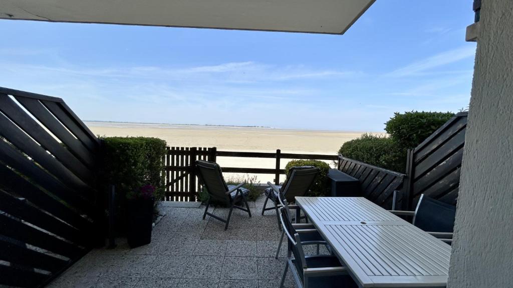 une terrasse avec une table et des chaises et la plage dans l'établissement Les Pieds dans le Sable – Appartement Unique avec Accès Direct à la Plage du Crotoy, au Crotoy