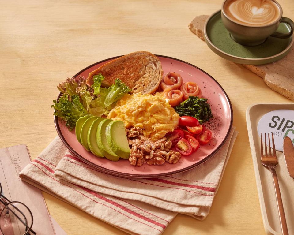 A colourful breakfast plate with scrambled eggs, avocado, salad, tomatoes, walnuts and toast.